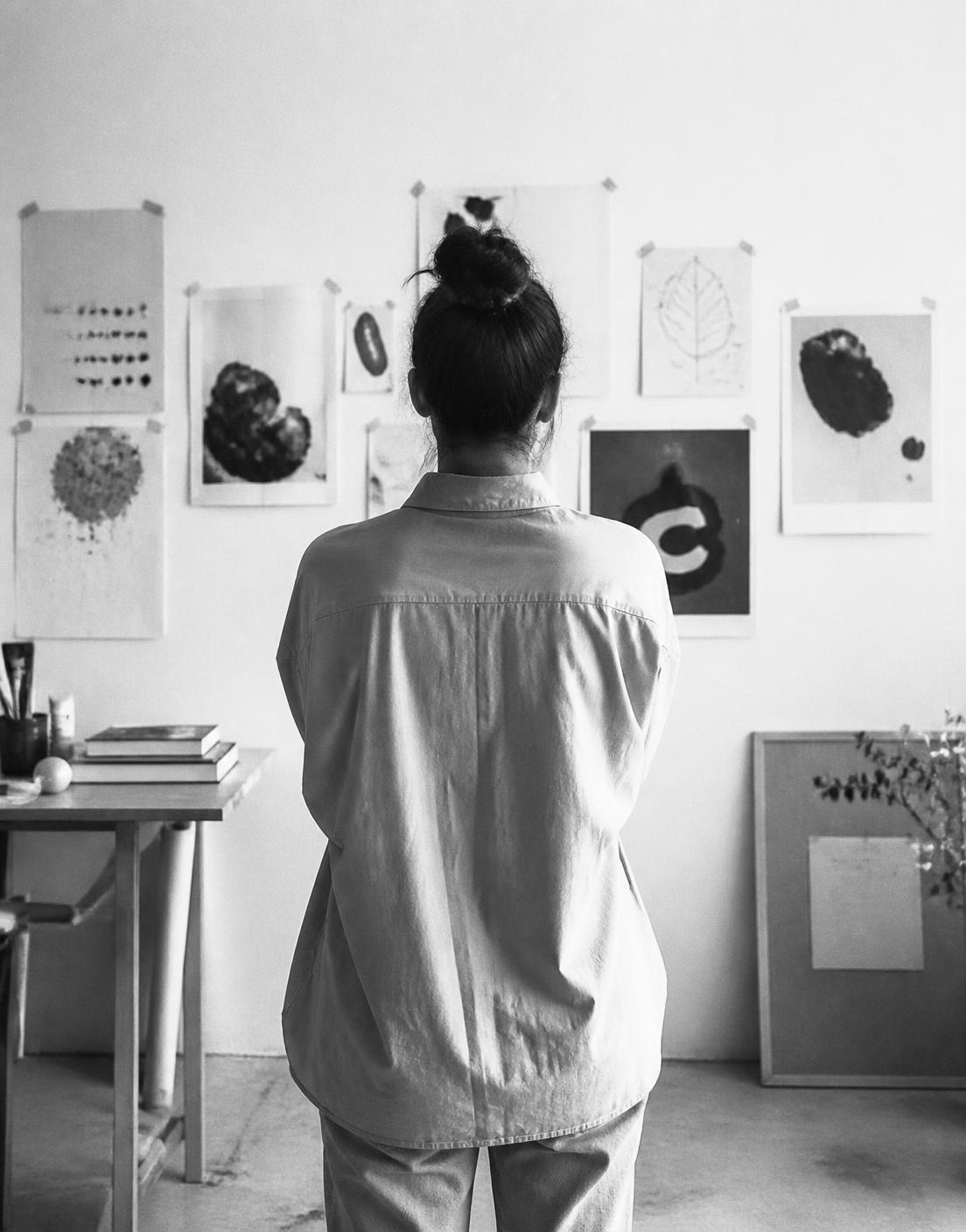 The designer in her studio, reviewing printed artwork pinned to the wall